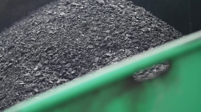 Close-up of fresh asphalt in a road paving machine. Detailed view of newly mixed asphalt material inside a modern roadwork paving machine. Captured showing texture and industrial technology.