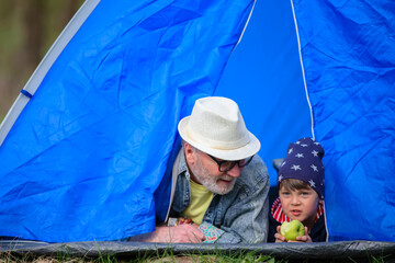 Grandfather and grandson are resting in a tourist tent in the forest. Active family recreation.