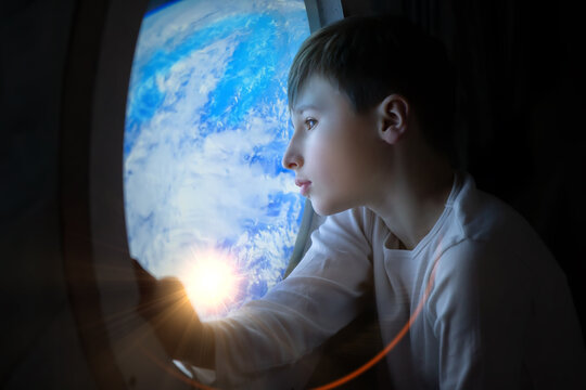 A boy is looking out of an airplane window at the Earth. The boy is looking at the sun, which is shining brightly - Powered by Adobe