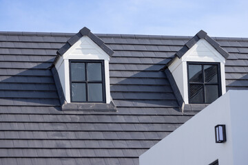 Two windows on a roof of garret house with a blue sky n the background