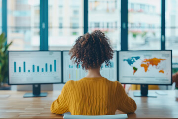 Businesswoman analyzing financial and world data on multiple computer monitors in a modern office with large windows.