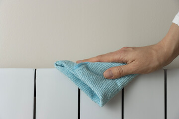 A woman's hand wipes dust from a heating radiator. White heater close-up. Cleaning with a blue cloth. Wet house cleaning