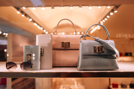 Front view of fancy Furla handbags and sunglasses on a stand in a shopping mall. Luxury accessories
