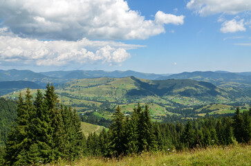 Scenic landscape view of rolling hills dotted with greenery and rural houses and layers of mountains receding into the distance on background under a vast sky with fluffy white clouds. Carpathians 