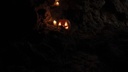 Fototapeta premium Walking Through a Dark Cave Approaching a Smiling and Scary-Eyed Halloween Pumpkin with Burning Candles Inside.