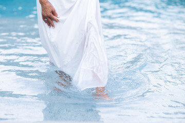 closeup of legs of woman in white flowing dress wading in the shallow end of an outdoor pool 