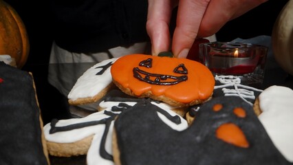 Drawing a Face with Black Icing on a Pumpkin-Shaped Cookie of Jack-o'-Lantern. Thematic Sweets in...