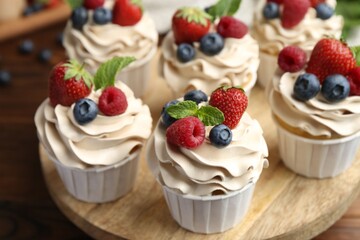 Tasty cupcakes with different berries and mint on wooden table, closeup