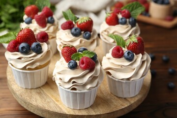Tasty cupcakes with different berries and mint on wooden table, closeup