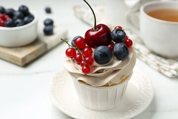 Tasty cupcake with different berries and tea on white marble table, closeup