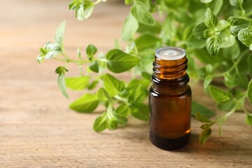 Essential oil in bottle and oregano twigs on wooden table, closeup