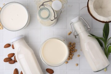 Different types of vegan milk and ingredients on white tiled table, flat lay