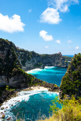 Tall cliff overlooking a blue ocean under a clear sky, surrounded by lush greenery.