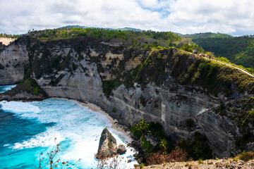Coastal beach with unique rock formations and blue ocean, surrounded by lush greenery.