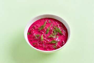 Cold summer beetroot soup in bowl on green background