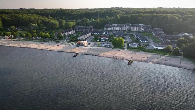 Aerial shot along fine sandy beach with a children's playground and beach volleyball court, promenade and holiday apartment residences at Wassersleben on the Flensburg Fjord near the Danish border.