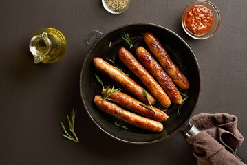 Delicious thin sausages in frying pan on brown background