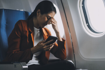 Stressed and serious young asian businesswoman remote working on the plane, suffering from headache and airsick during the flight.