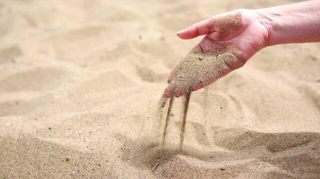 Close up of woman pouring sand running through fingers slow motion at the beach with sun flare.