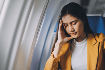 Young asian chinese airplane passenger woman experiencing discomfort, Airplane headache. Worried female passenger holding head, feeling unwell Anxiety and fear in the skies. Stressful travel moments.