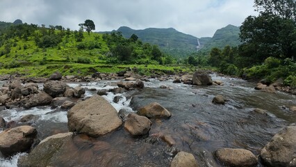 Scenic view of mountain stream cascading over rocks with green hills in the backdrop.