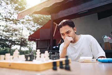 A Southeast Asian man is confused while playing chess in the afternoon at a traditional coffee shop