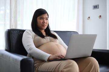 Happy pregnant woman with big tummy relax at home. Portrait of pregnant mature woman standing near the window and caresses her belly. Smiling woman expecting child and looking at camera.