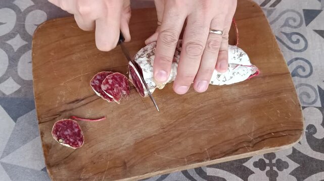 gros plan sur les mains d'une homme coupant un saucisson