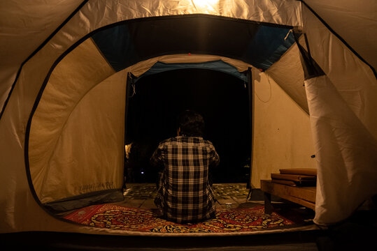 A man camping and sitting alone inside the tent at night