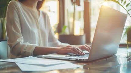 Fototapeta premium A person working on a laptop in a bright, modern workspace, surrounded by greenery and natural light.