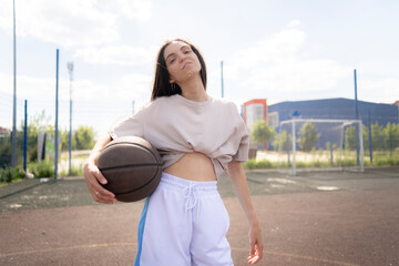professional female basketball player, dressed in athletic clothing, stands on an outdoor court holding a basketball