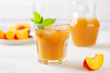 Peach and nectarine ice tea in a glass with mint on white table. Juice, cocktail, lemonade made from peach.