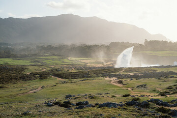 A large body of water with a small waterfall in the foreground. The water is misty and the sky is cloudy