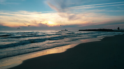 A tranquil sunset over a calm sea with birds in flight and a lighthouse silhouette