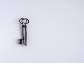 Two rusty iron keys hang on a nail on a white wall.
