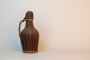 Close-up detail of a vintage glass bottle covered in intricate woven rattan or wicker casing, tied with natural twine around the neck. This traditional craft packaging is used for drinks or oil