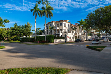 Fototapeta premium A street corner in a wealthy neighborhood in downtown Naples, with a large white building, palm trees, and a few cars on a sunny day.
