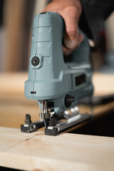 man cutting a wooden plank with electric jigsaw in a workshop