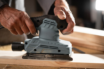 Close-up of sending a wood with electric sander at workshop.