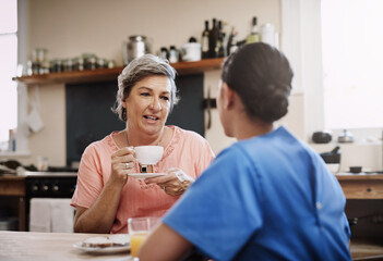 Obraz premium Senior woman, nurse and kindness in kitchen for consultation, therapy and mental health. Tea, discussion and retired female person with medical worker or caregiver in home for conversation and advice
