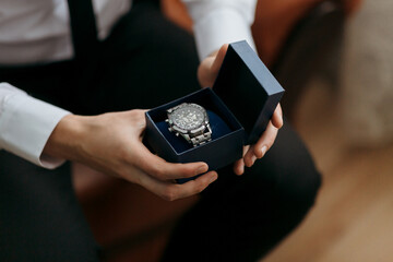A man is holding a watch in a box. The watch is silver and black. The man is wearing a suit and tie. The watch is a gift for someone special