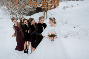 A bride and her bridesmaids are posing for a picture in the snow. The bride is wearing a white gown...