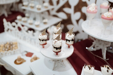 A dessert table with a variety of desserts, including a white plate with three desserts in clear plastic cups
