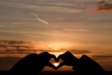 Silhouette main en forme de cœur sur coucher de soleil