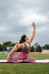A young sporty woman doing her morning workout, practicing yoga exercises on the stadium field, side view