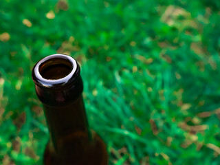 The neck of a wine or beer bottle made of brown glass on a background of green lawn grass