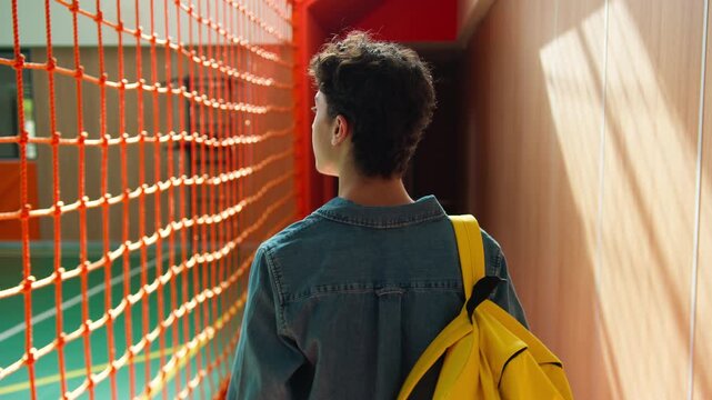Back view from behind unrecognizable Caucasian student guy boy school pupil male man teen schoolboy teenager with schoolbag backpack walking in sport hall university college walk go education studying