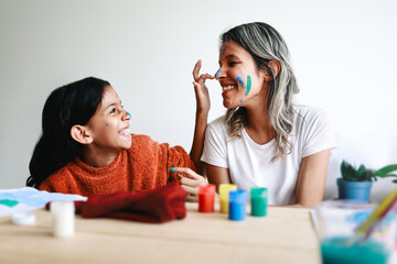 Happy Latin mother and daughter having fun painting each other face at home. Family, mom and kid...