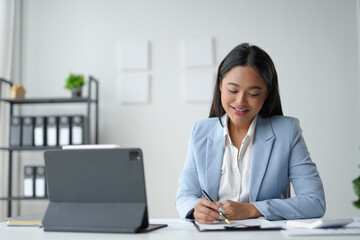 Young asian businesswoman working with documents and smiling at her desk in a modern office
