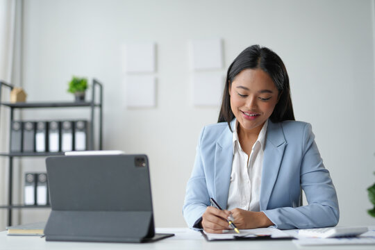 Young asian businesswoman working with documents and smiling at her desk in a modern office